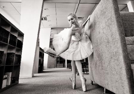 ballerina on pointe shoes in the library reads a book holding it up