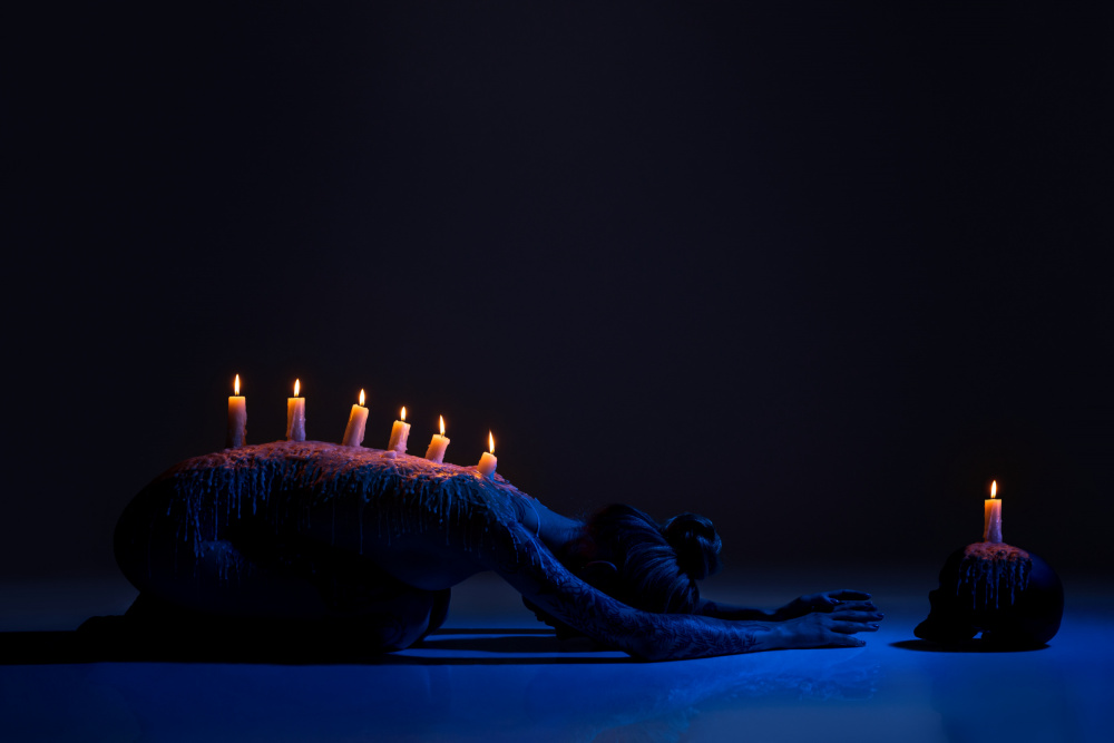 Burning candles on back of lady bowing down in darkness à Andrey Guryanov