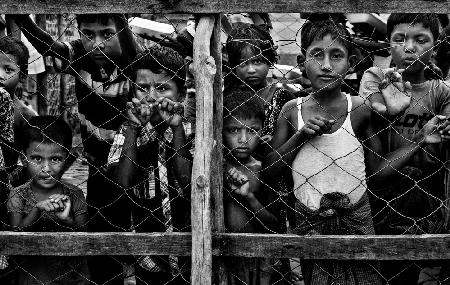 Rohingya children observing the distribution of food in boxes to other children.