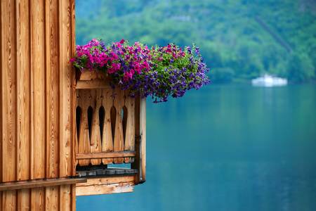 Blick auf einen Holzbalkon mit Petunien, im Hintergrund der Hallstaettersee